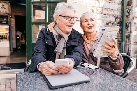 An elderly couple is sitting at a table looking at a map and a cell phone.