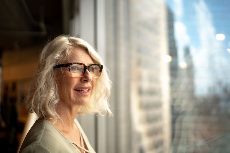 A woman wearing glasses is looking out of a window.