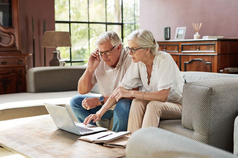 An elderly couple is sitting on a couch looking at a laptop.