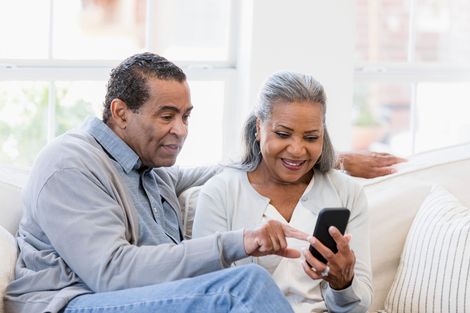 An elderly couple is sitting on a couch looking at a cell phone.