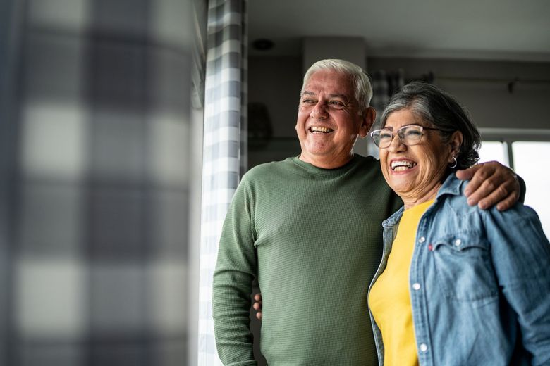 An elderly couple is standing next to each other in front of a window.