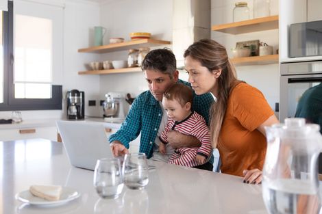 A family is sitting at a kitchen counter looking at a laptop.