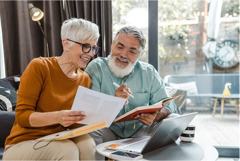 A man and a woman are sitting on a couch looking at papers and a laptop.