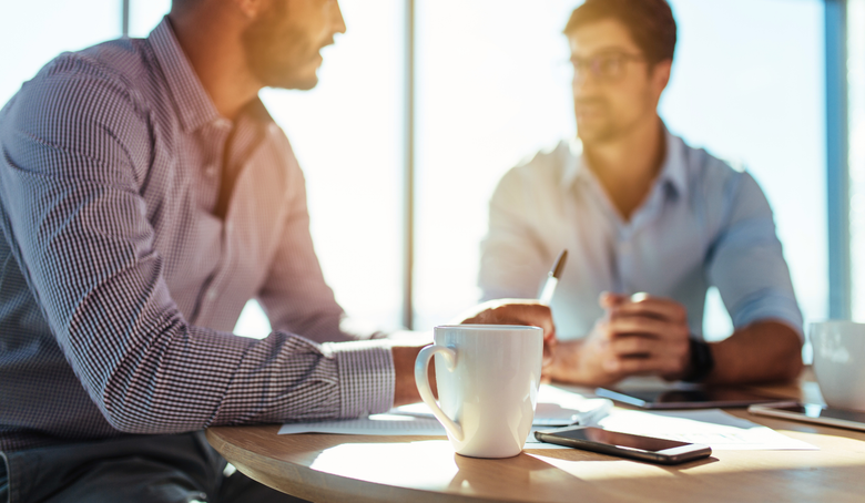 Two men are sitting at a table talking to each other.