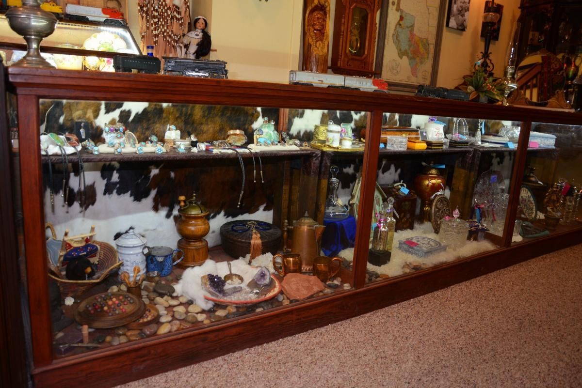 A long, wooden display case filled with various items, against a cowhide background, on a carpeted floor.