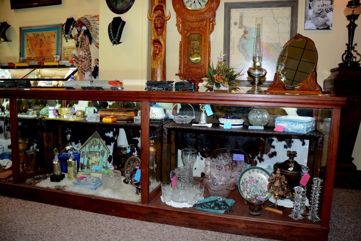 Antique shop display case filled with glassware, figurines, and other vintage items, with a wooden cabinet.