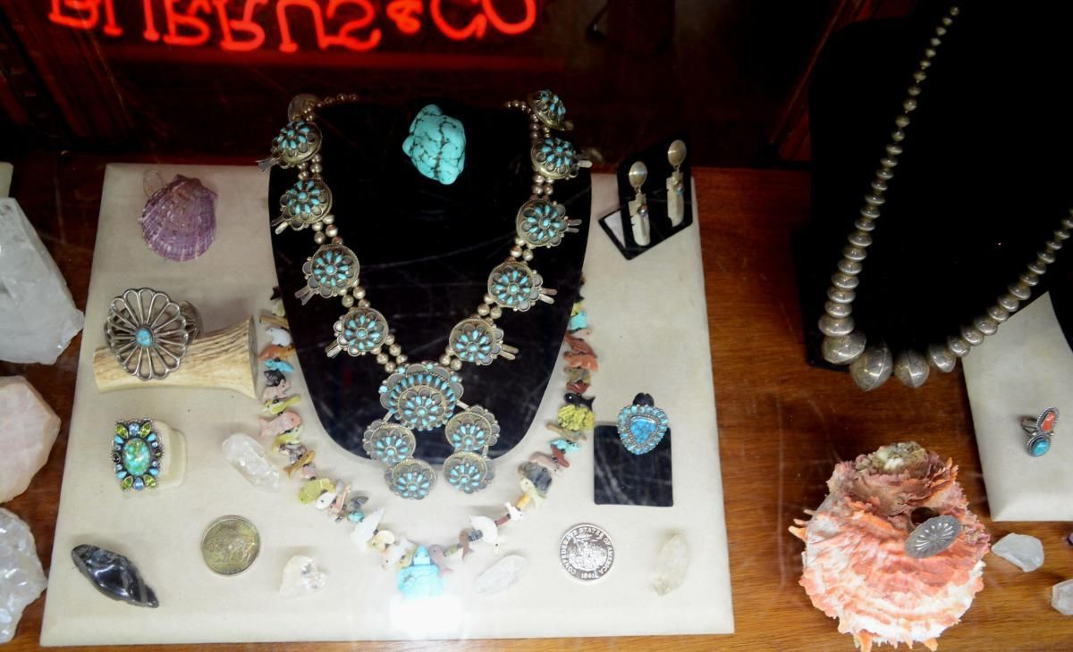 Jewelry display case with turquoise necklaces, earrings, and rings on a beige surface.