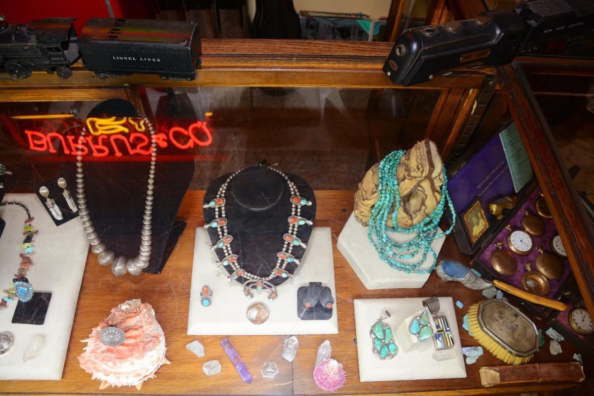 Jewelry display in a glass case, with necklaces, earrings, and other items lit by a neon sign.