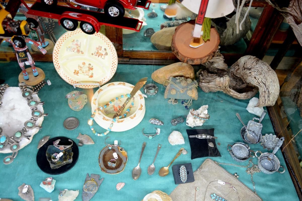 Display case with turquoise jewelry, pottery, and small figurines on a teal cloth.
