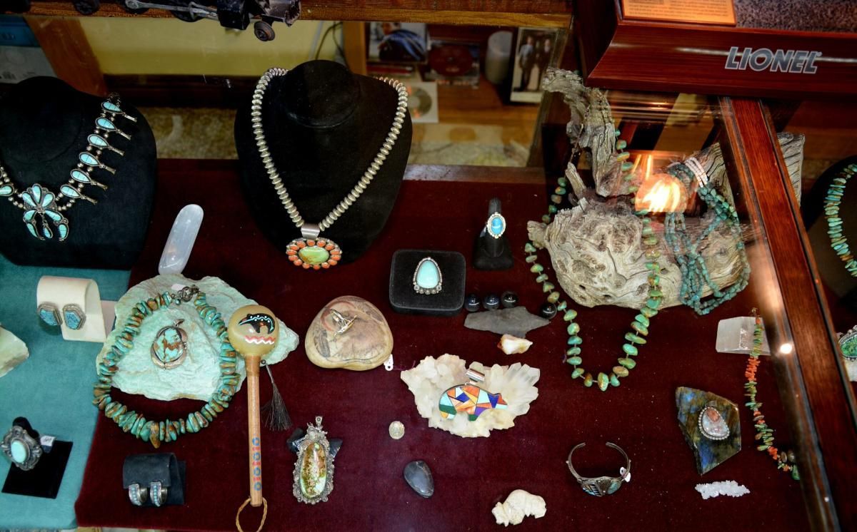 Jewelry display case with turquoise necklaces, rings, and other decorative items on a dark red surface.