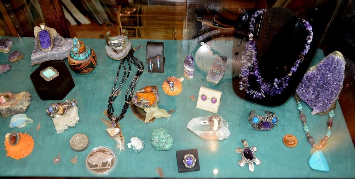 Jewelry display case with necklaces, rings, and gems in various colors: purple, orange, turquoise, and silver.