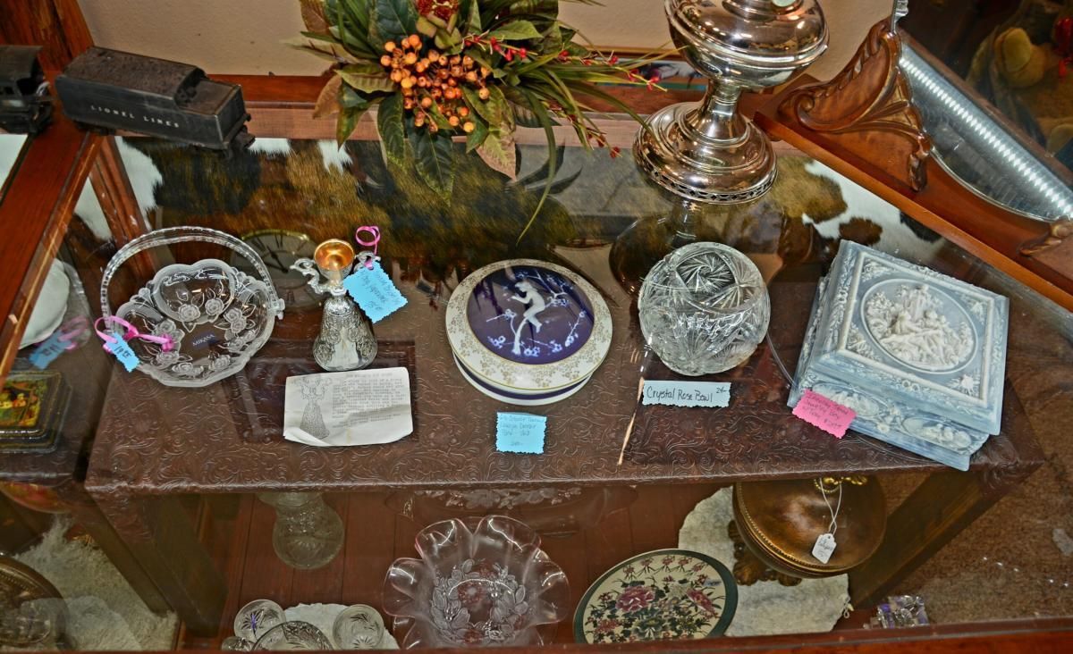 Display case with various antique items: glass bowl, box with blue lid, ornate silver pieces.