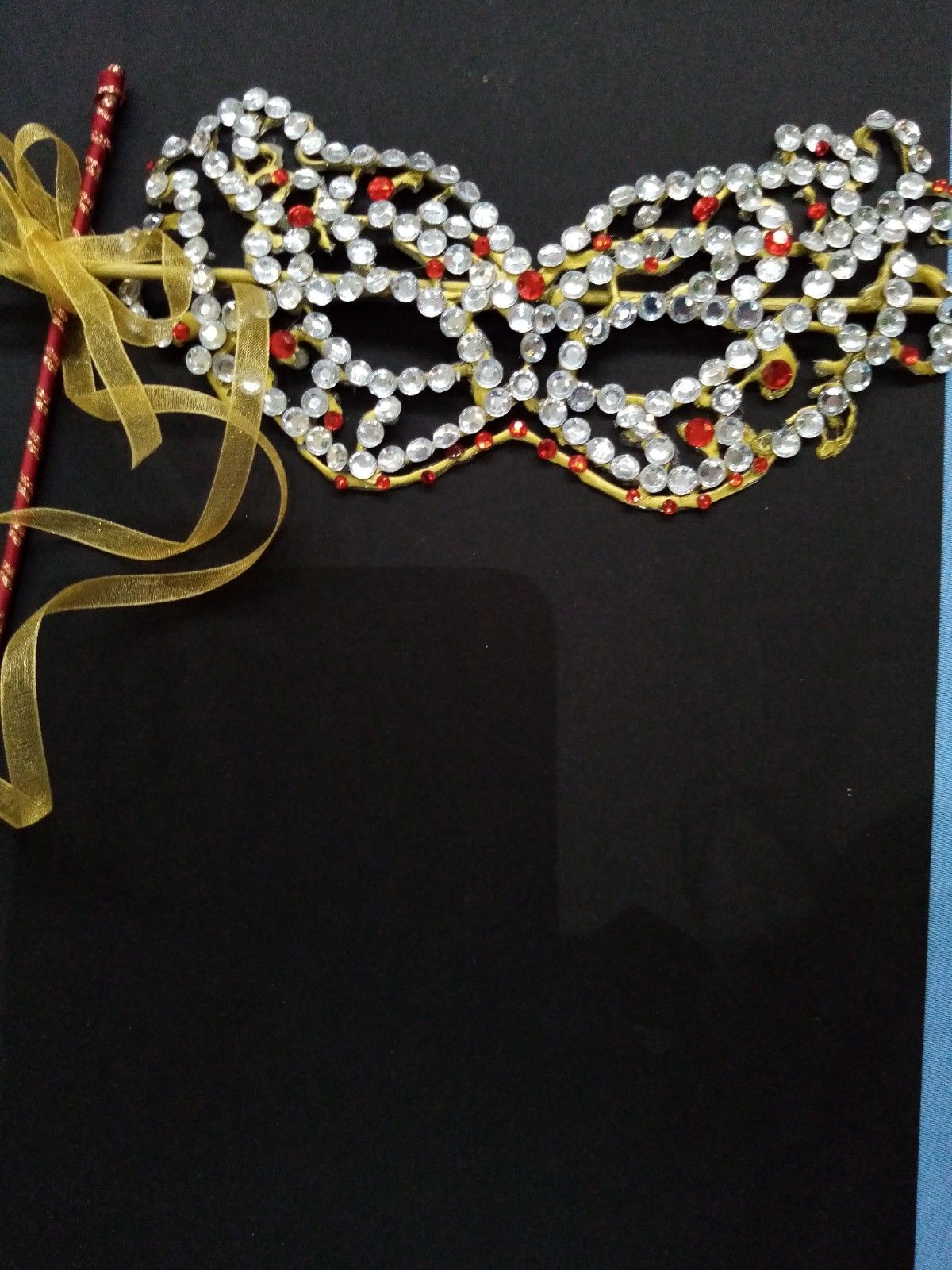 A mask with rhinestones and ribbon on a stick