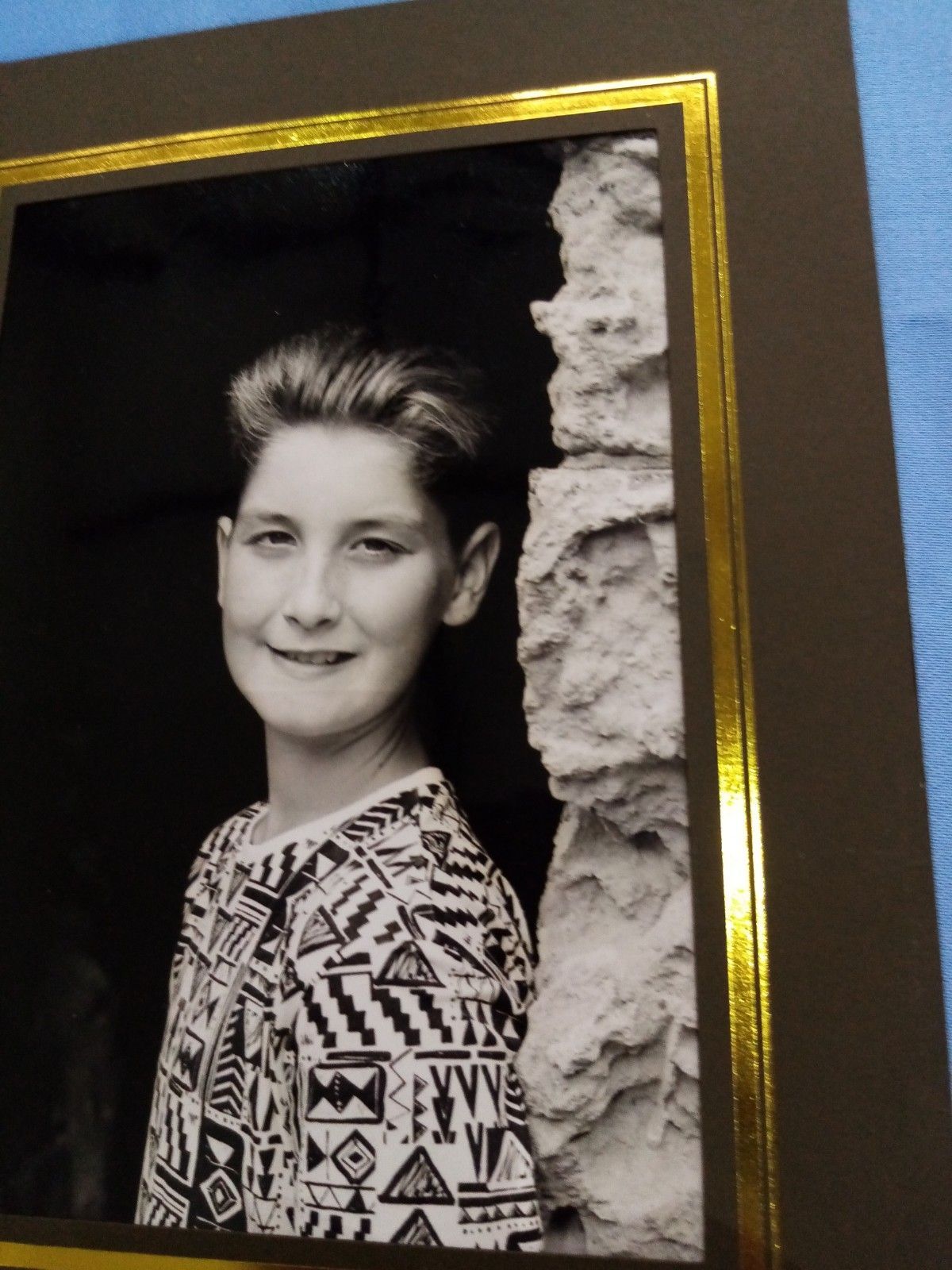 A black and white photo of a young boy standing next to a stone wall