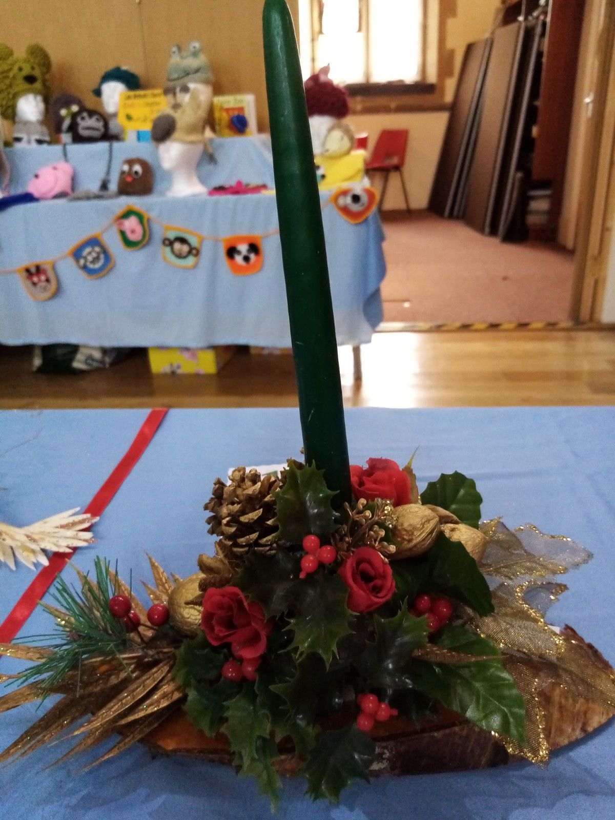 A green candle is surrounded by flowers and pine cones