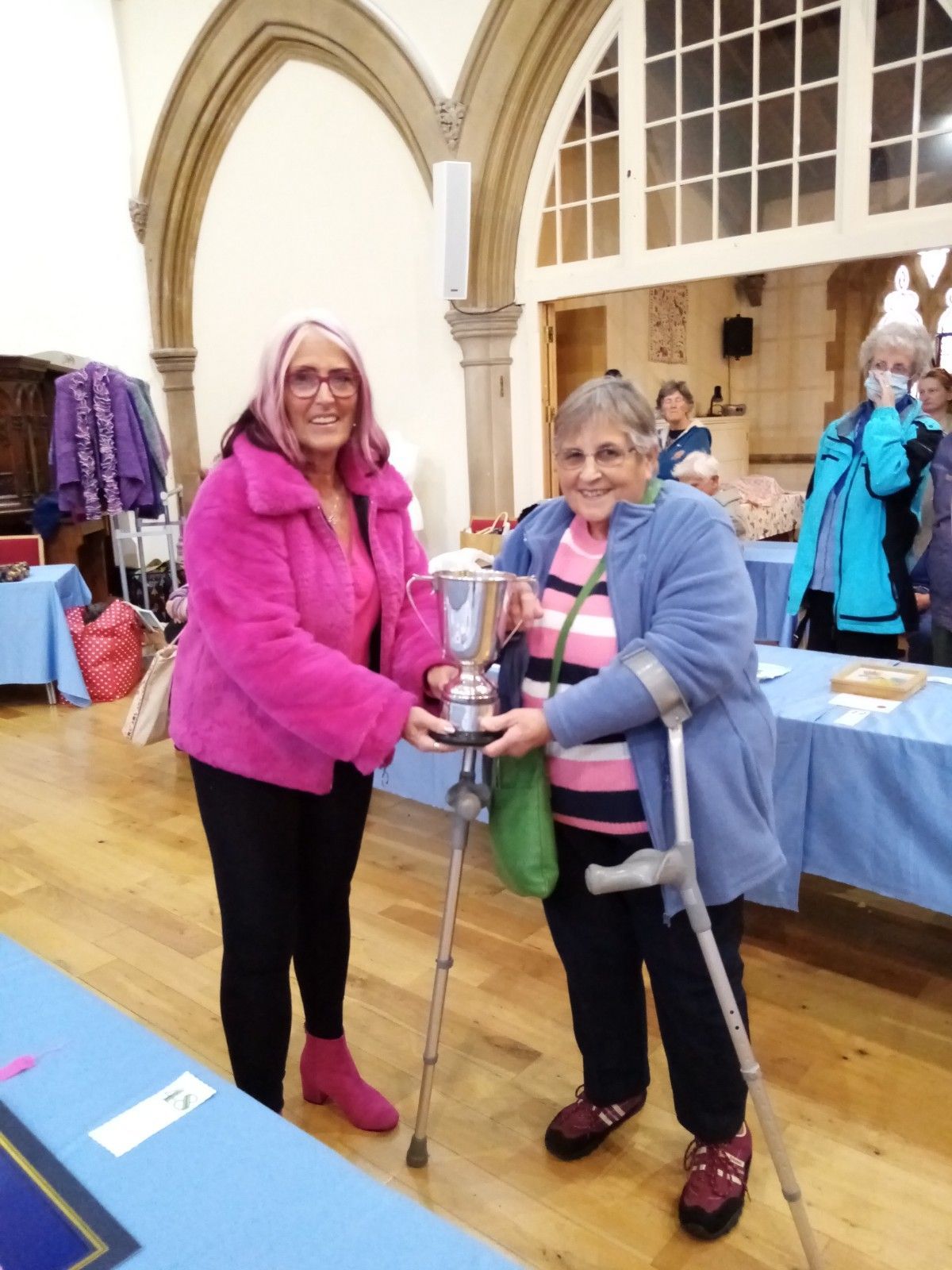 A woman with crutches is holding a trophy next to another woman