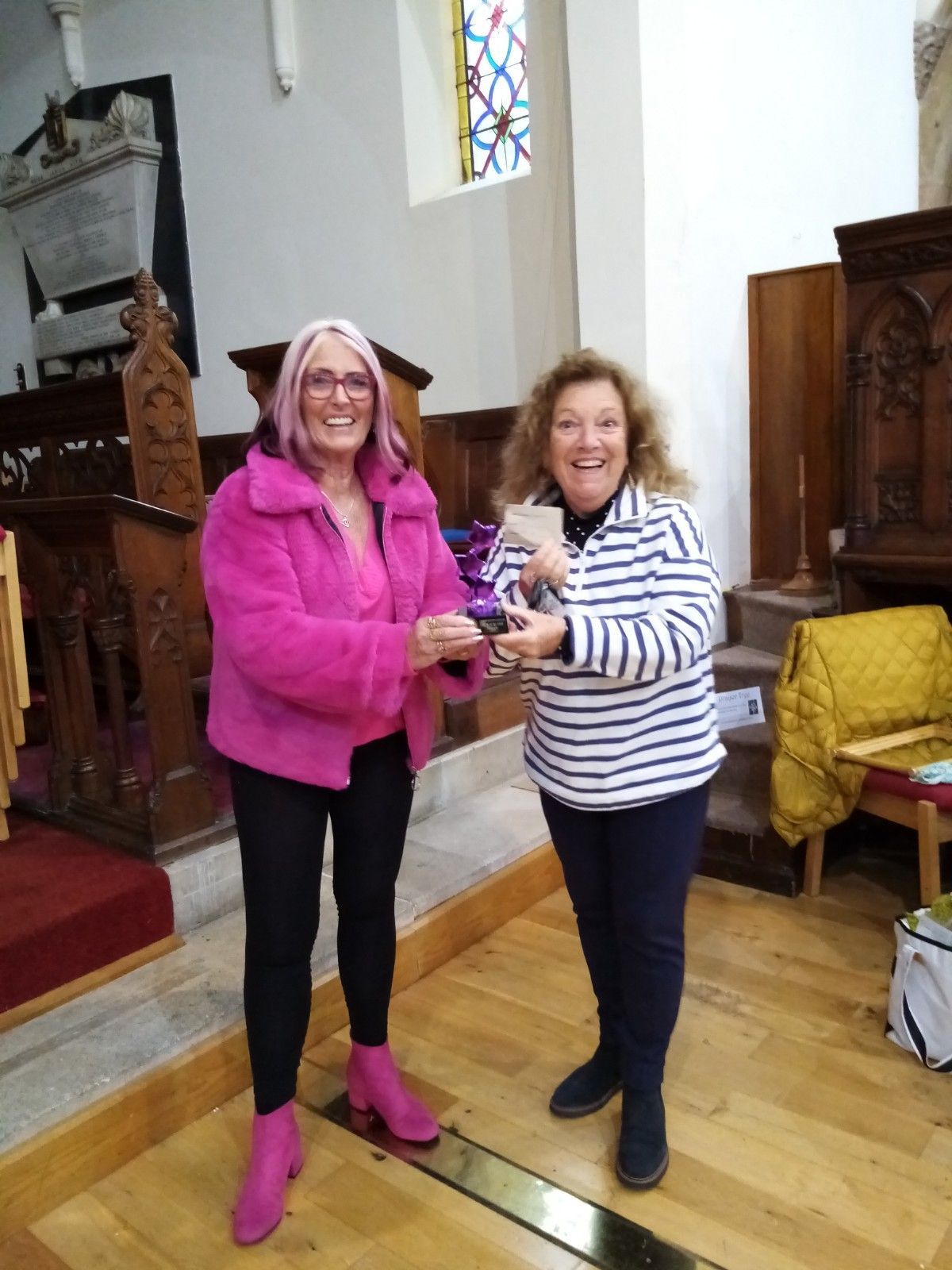 Two women are standing next to each other in a church and one of them is wearing a pink jacket.
