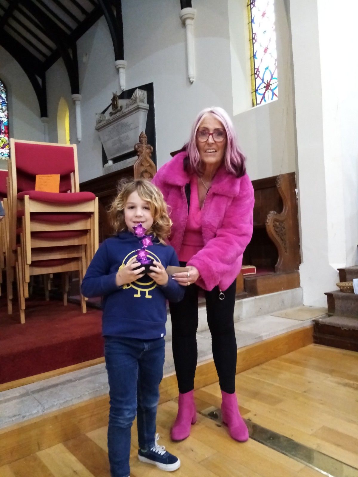 A woman with pink hair is standing next to a little boy in a church