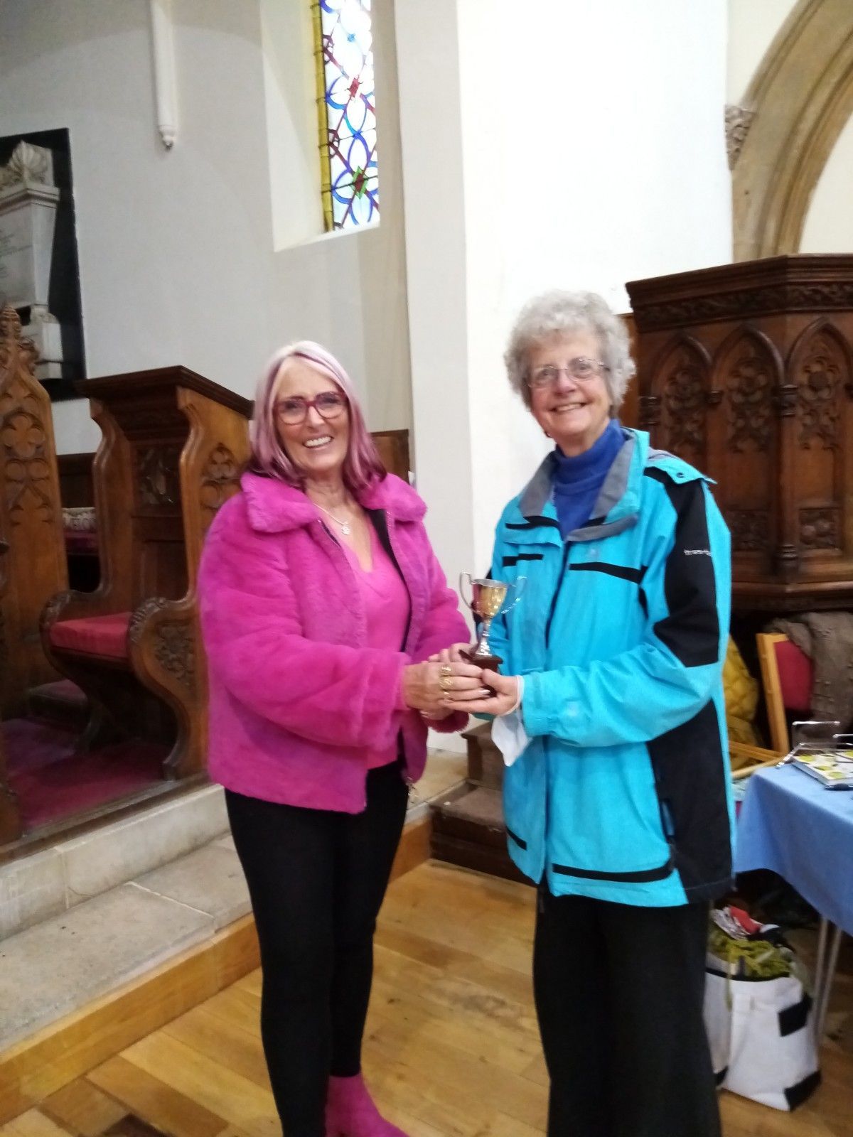 A woman in a pink jacket is giving a trophy to another woman in a blue jacket