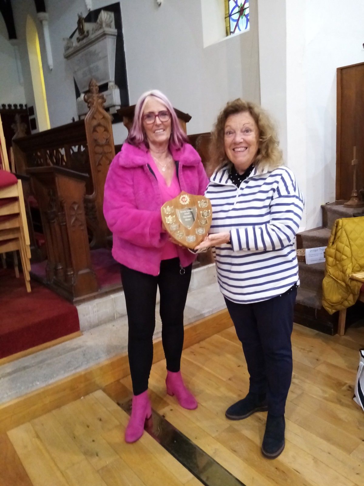 Two women are standing next to each other in a church holding a heart shaped plaque.
