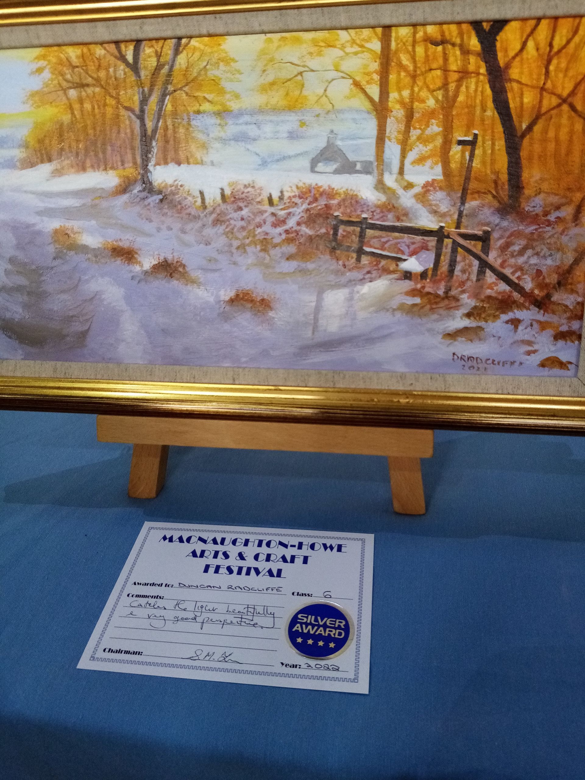 A framed painting of a snowy forest is on an easel