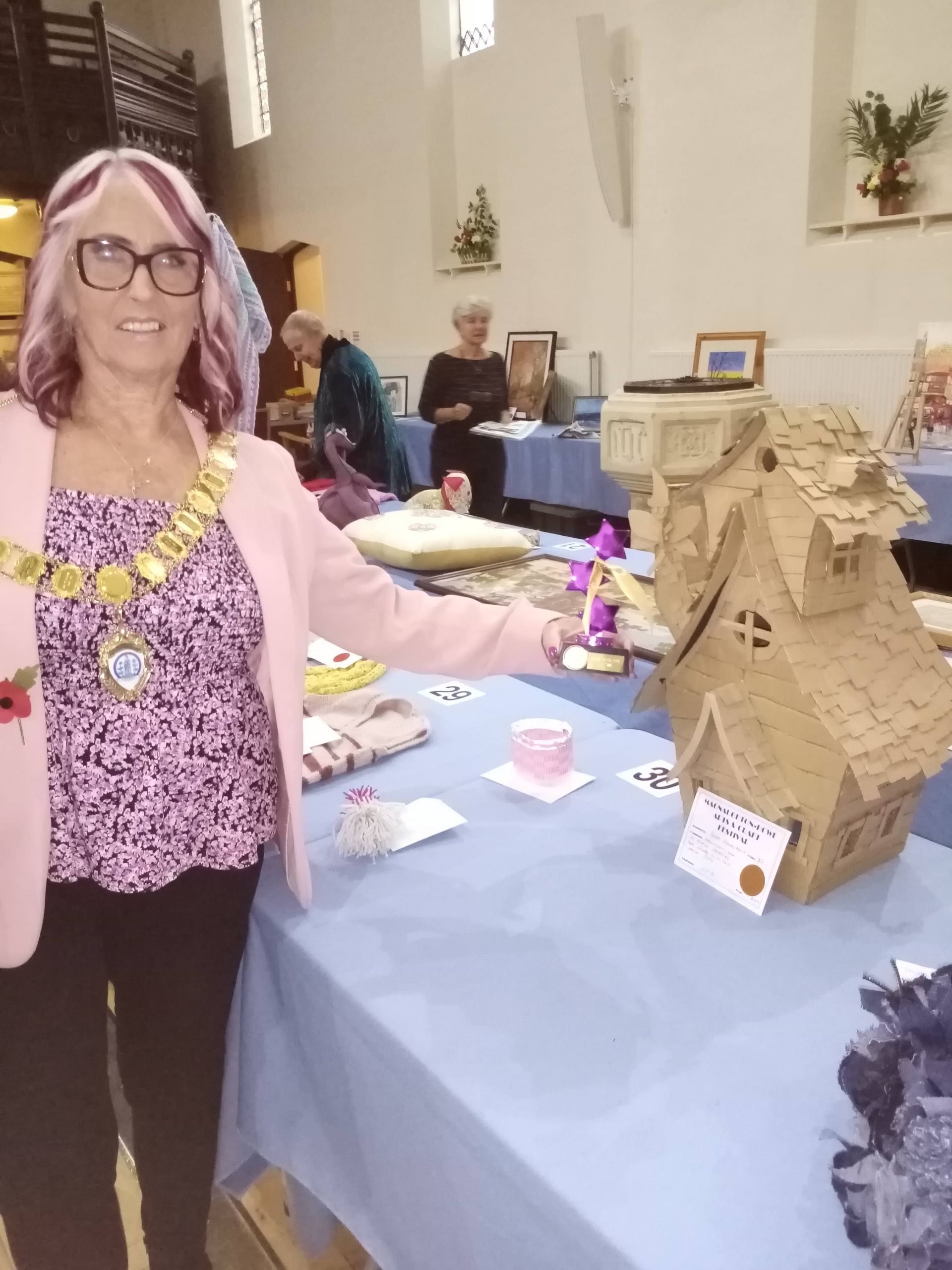 A woman is standing in front of a table with a cardboard house on it