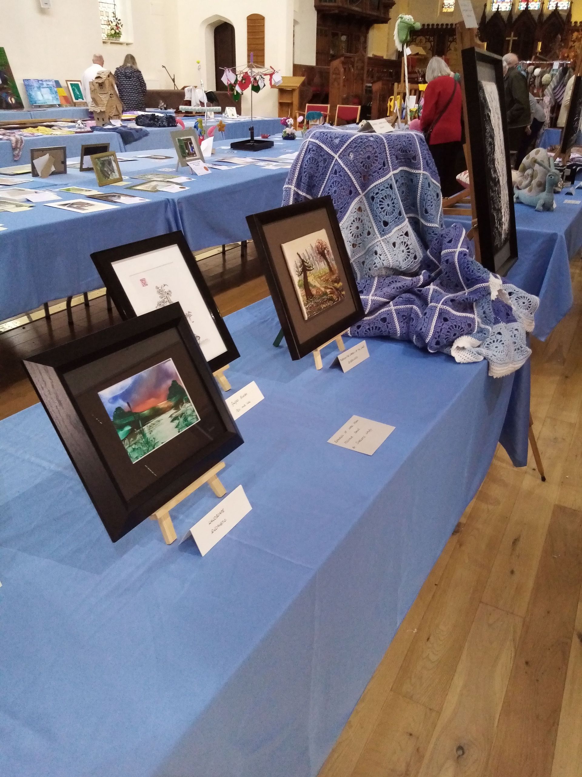 Several paintings are displayed on a table with a blue table cloth