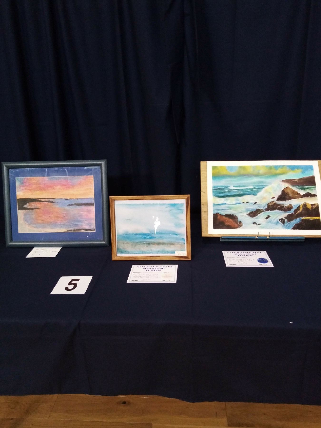 Three paintings are on a table with the number 5 on it