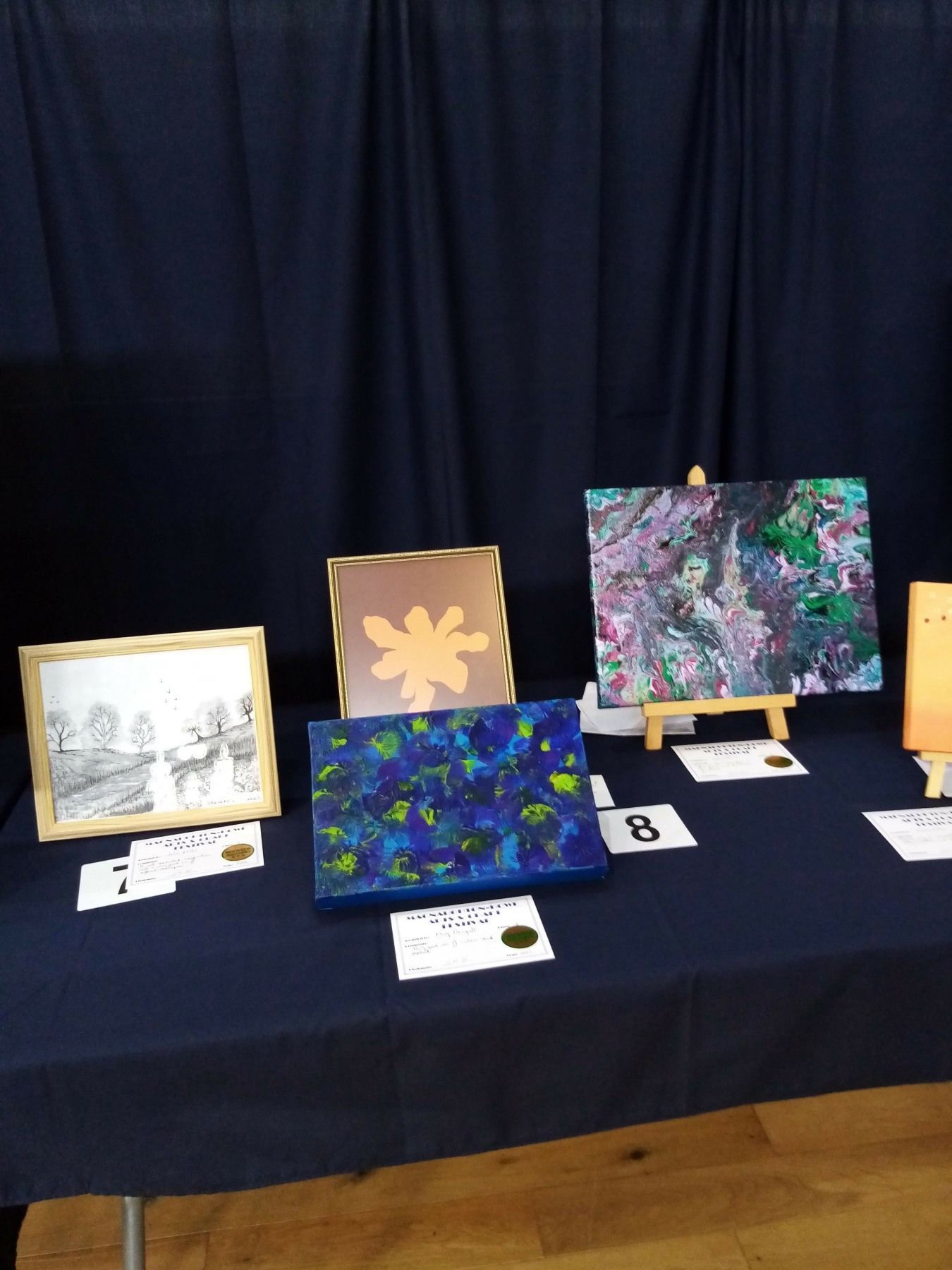 Several paintings are on display on a table including one with the letter b on it