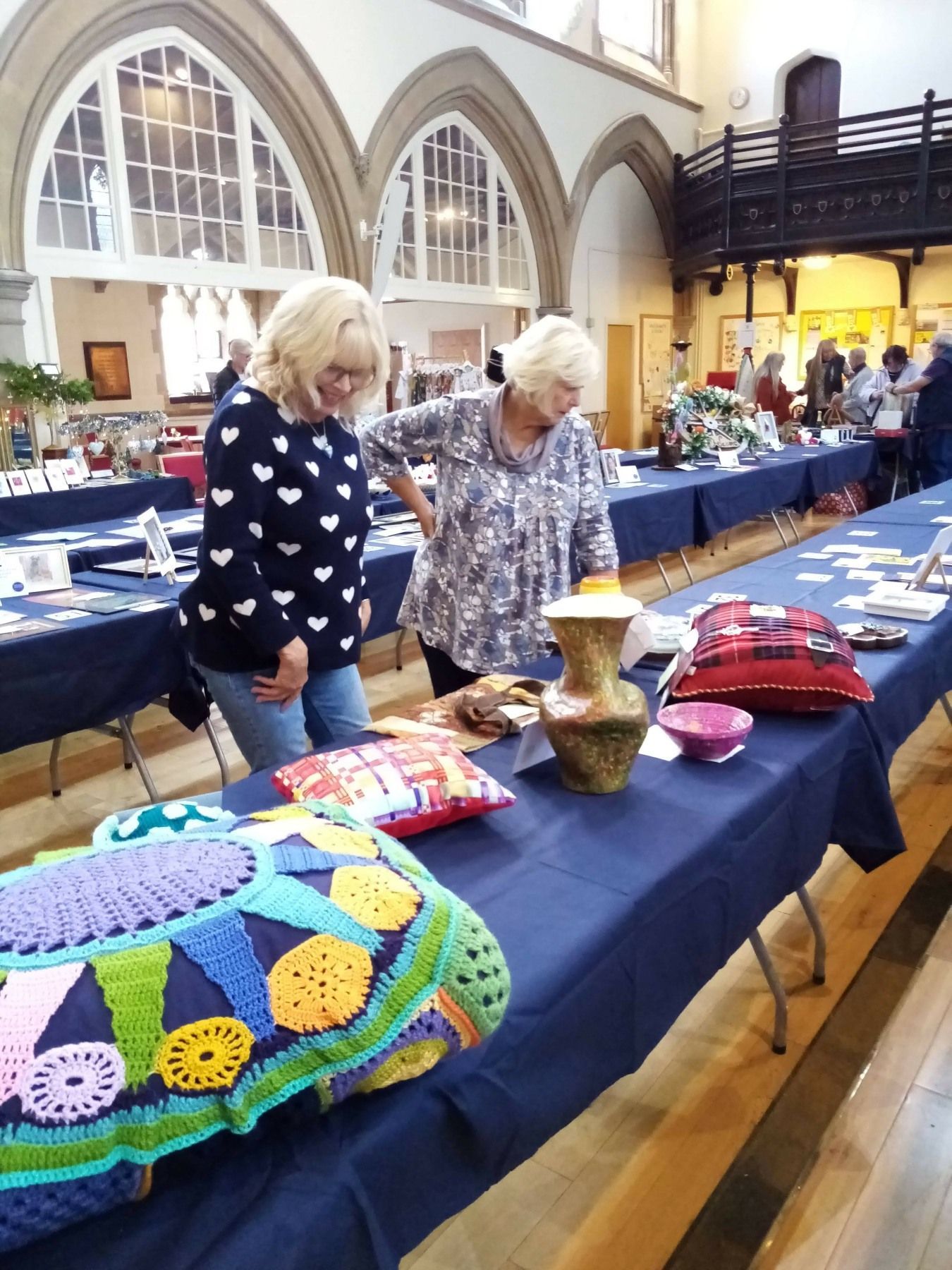 Two women are looking at a table with crocheted items on it