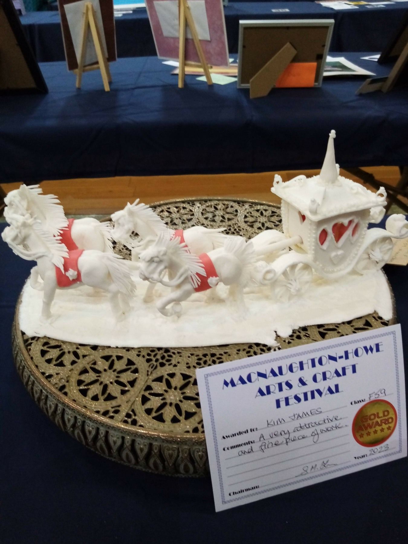 A statue of a horse drawn carriage is on a table with a certificate that says macnallt tensileme arts & craft festival