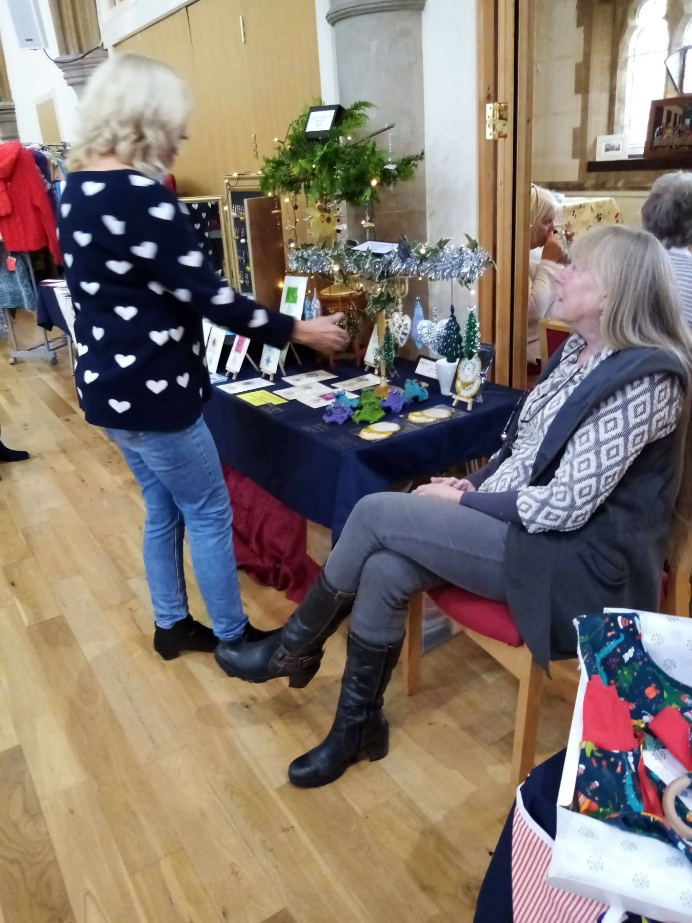A woman is standing next to a woman sitting at a table.