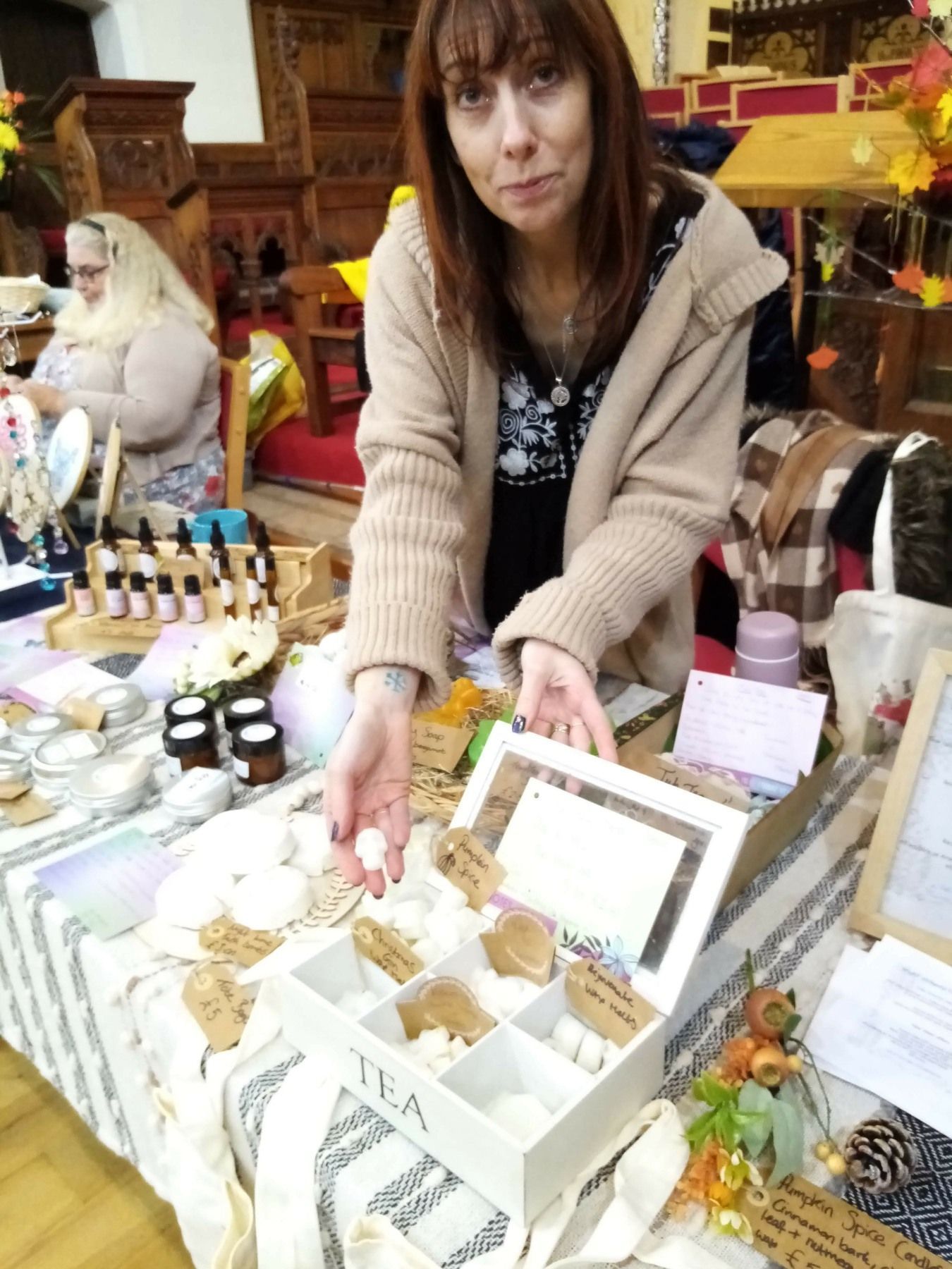 A woman is standing in front of a table holding a small white box.