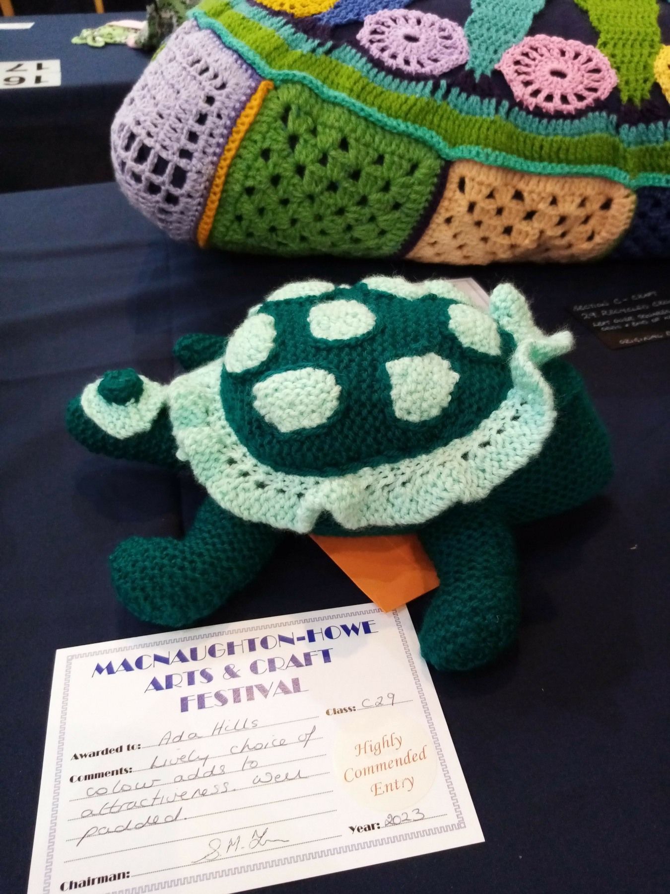 A crocheted turtle sits on a table next to a certificate
