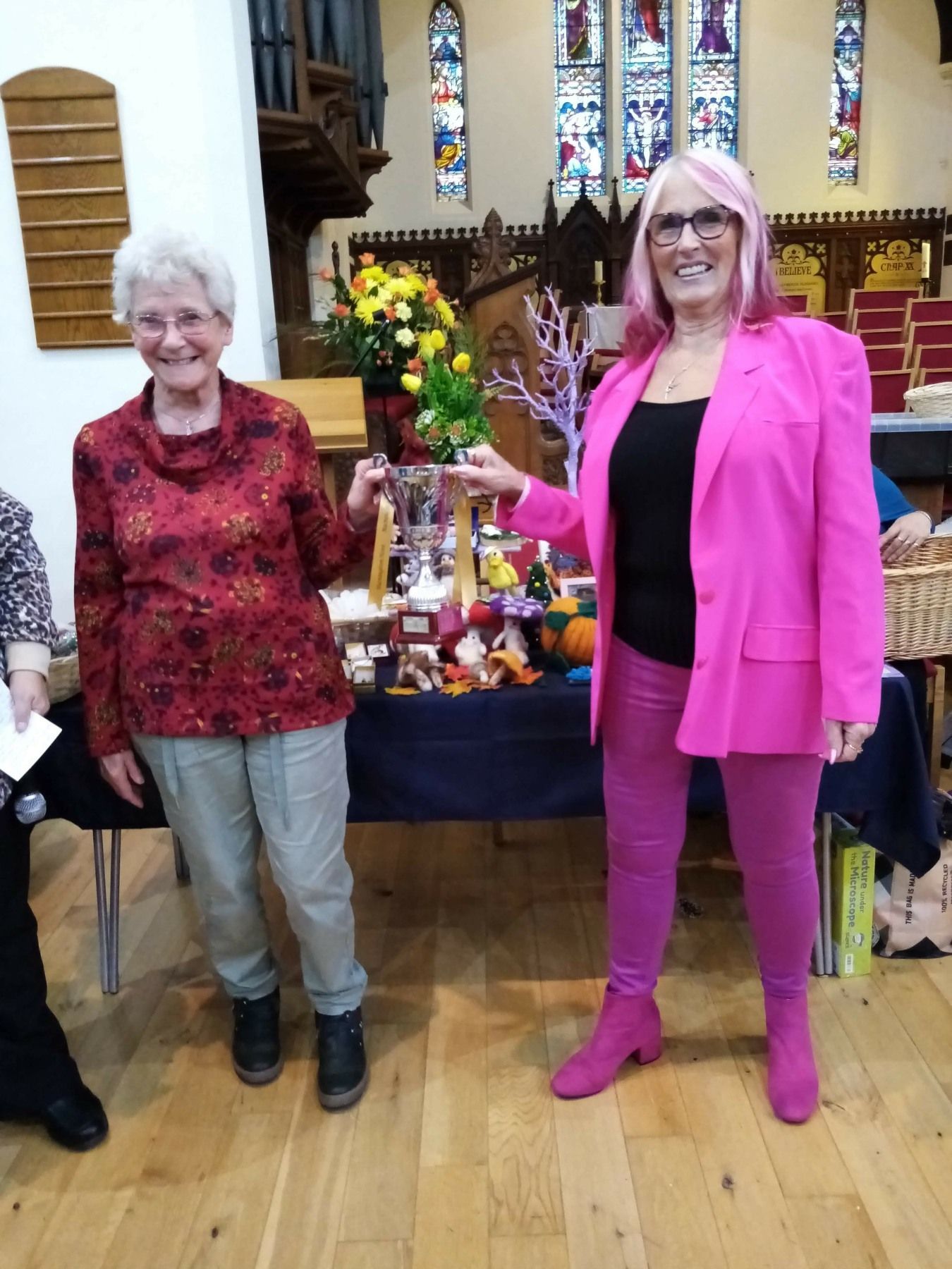 Two women are standing next to each other in a church . one of the women is wearing a pink jacket.