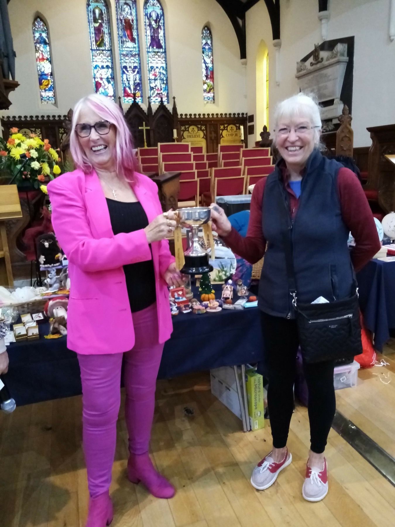 Two women toasting in a church with stained glass windows in the background