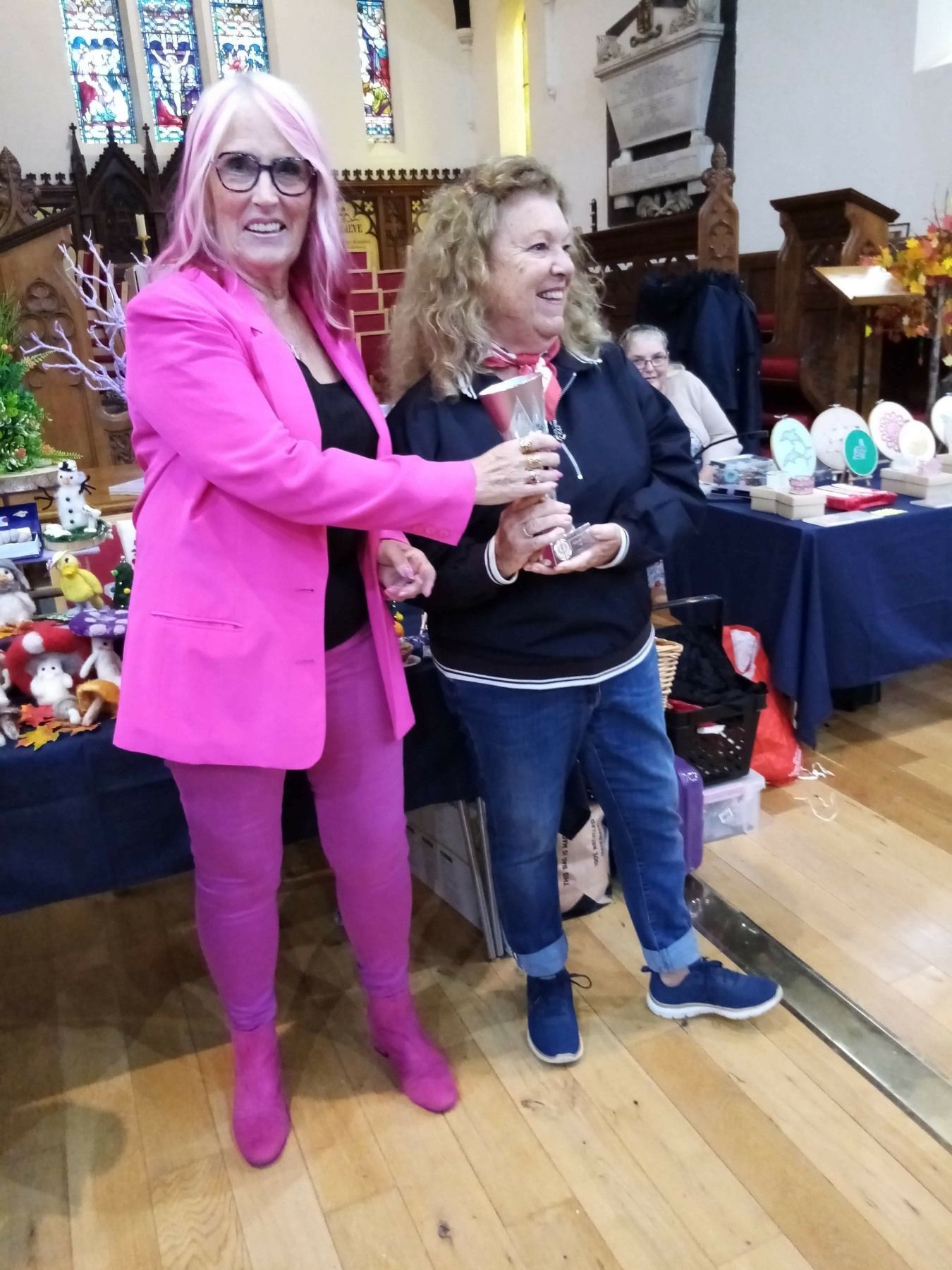 Two women are standing next to each other on a wooden floor holding a vase.