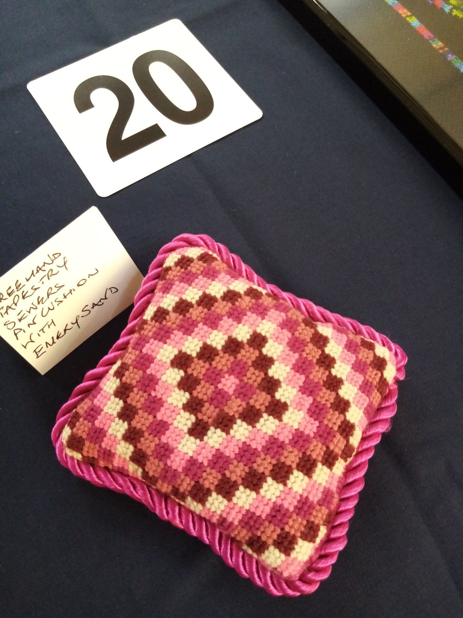 A cross stitched pillow sits on a table next to a number 20
