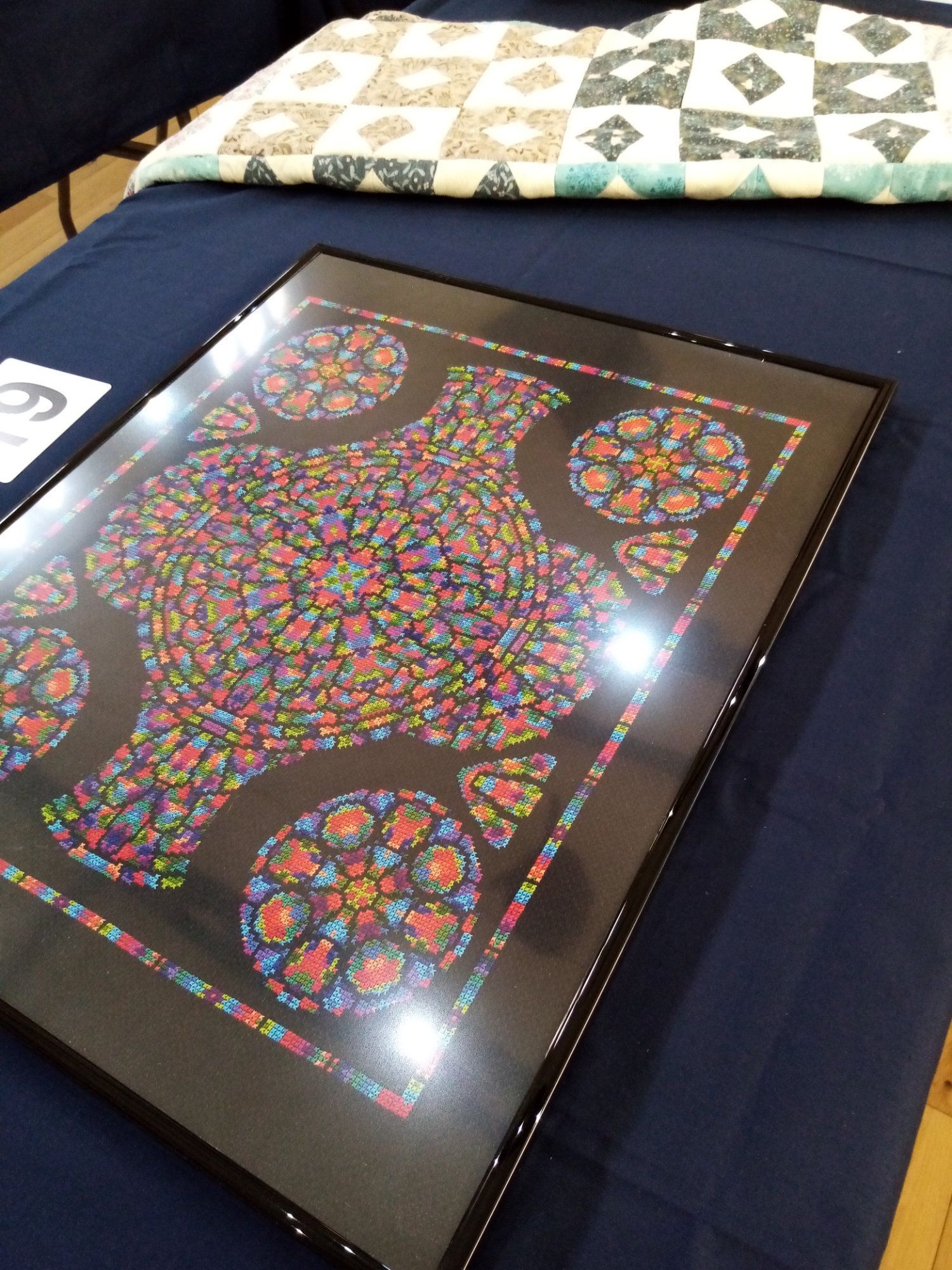A framed picture of a bird is on a table next to a quilt