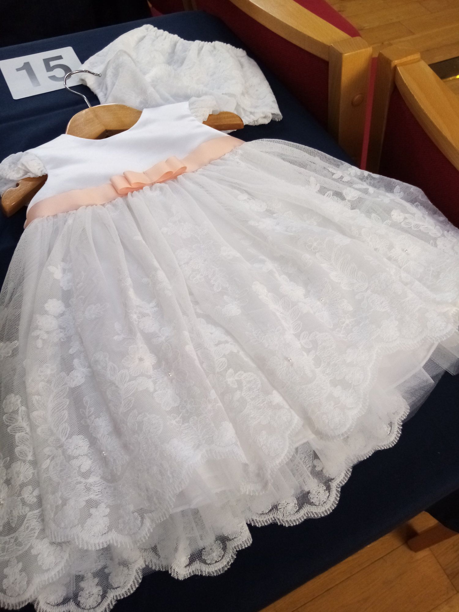 A white lace dress with a pink ribbon sits on a table with the number 15 on it