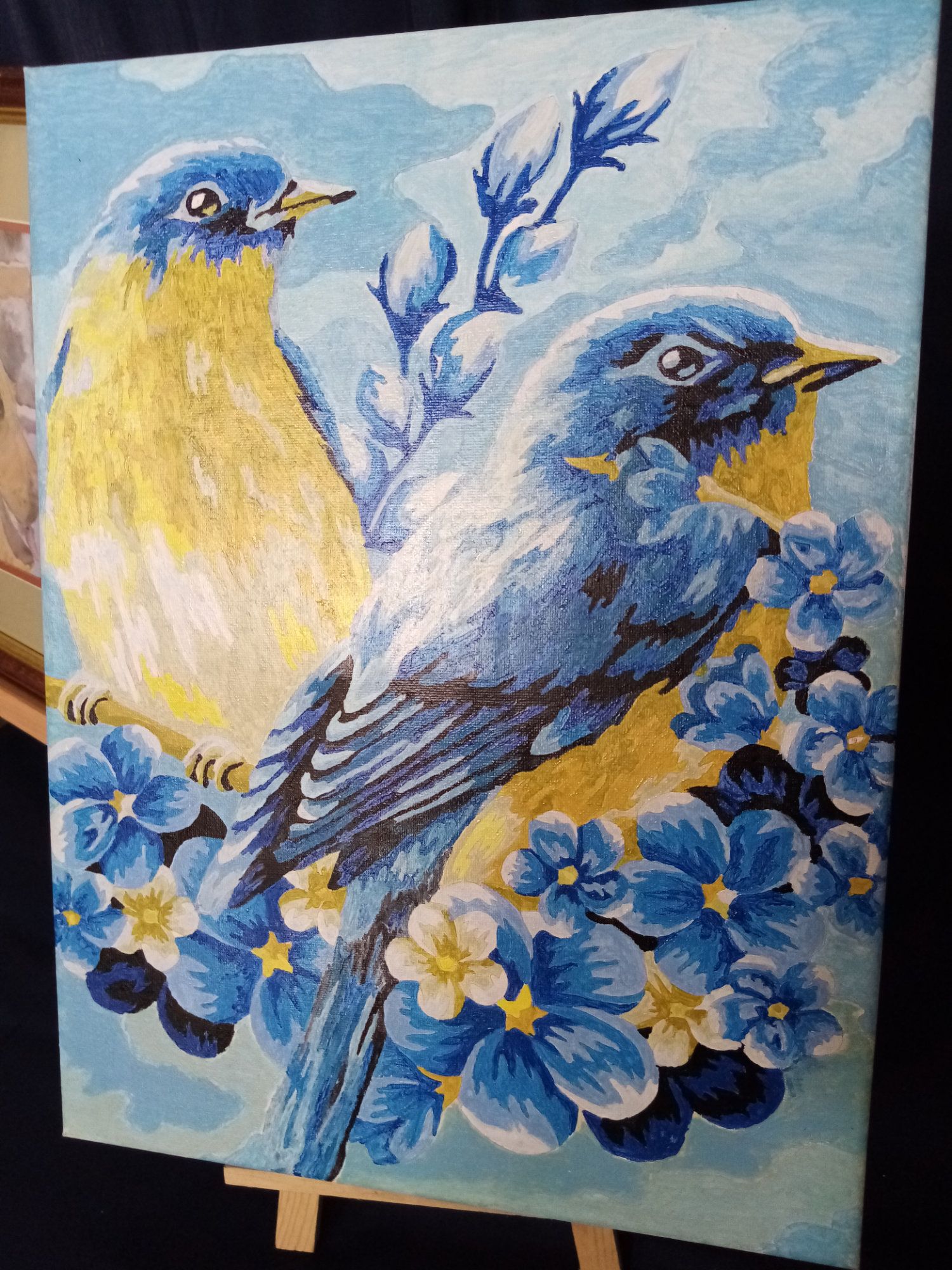 A painting of two birds sitting on a branch with blue flowers