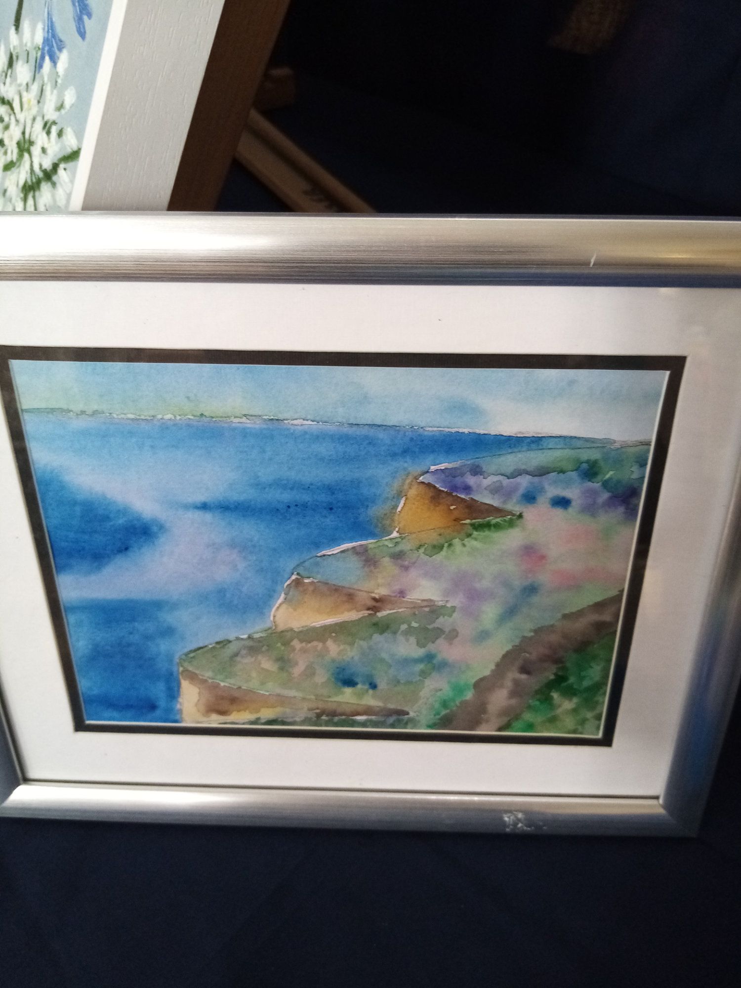 A framed watercolor painting of a cliff overlooking the ocean