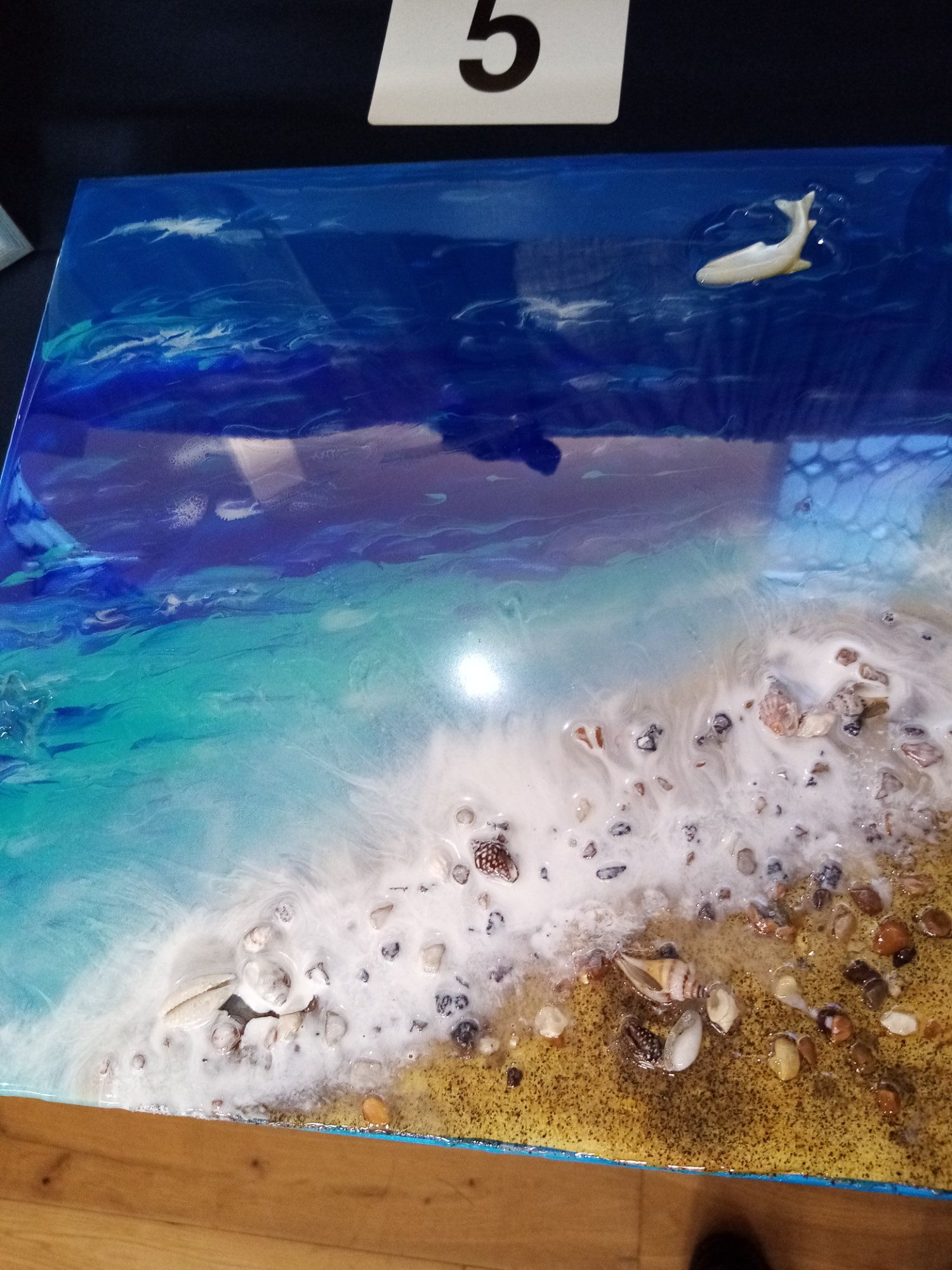 A painting of a beach with waves and shells on a wooden table.