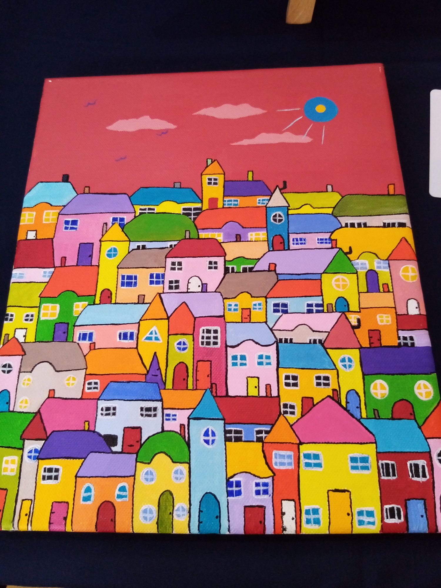 A painting of colorful houses with a blue balloon in the sky