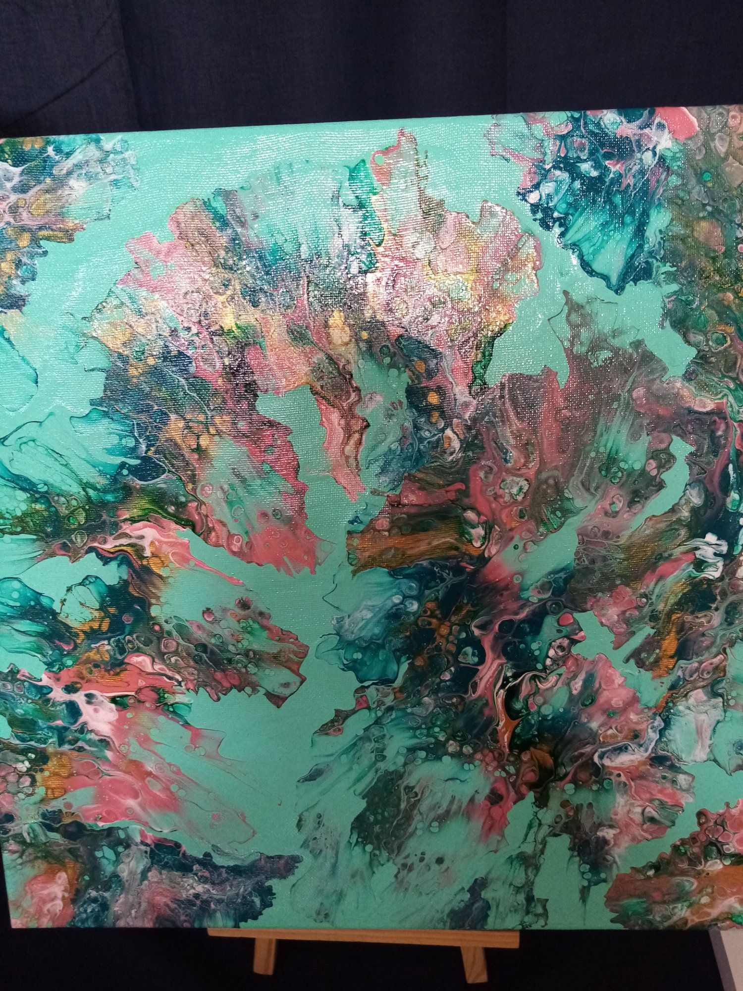 A colorful painting is sitting on a wooden easel.