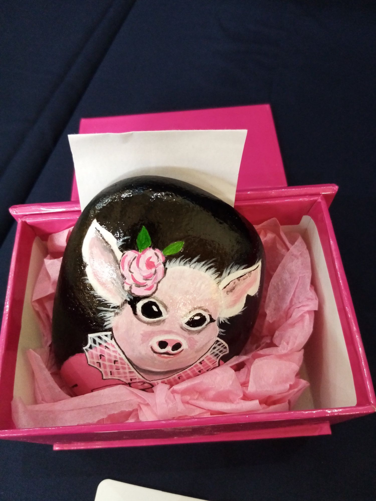 A rock with a picture of a pig on it is in a pink box.