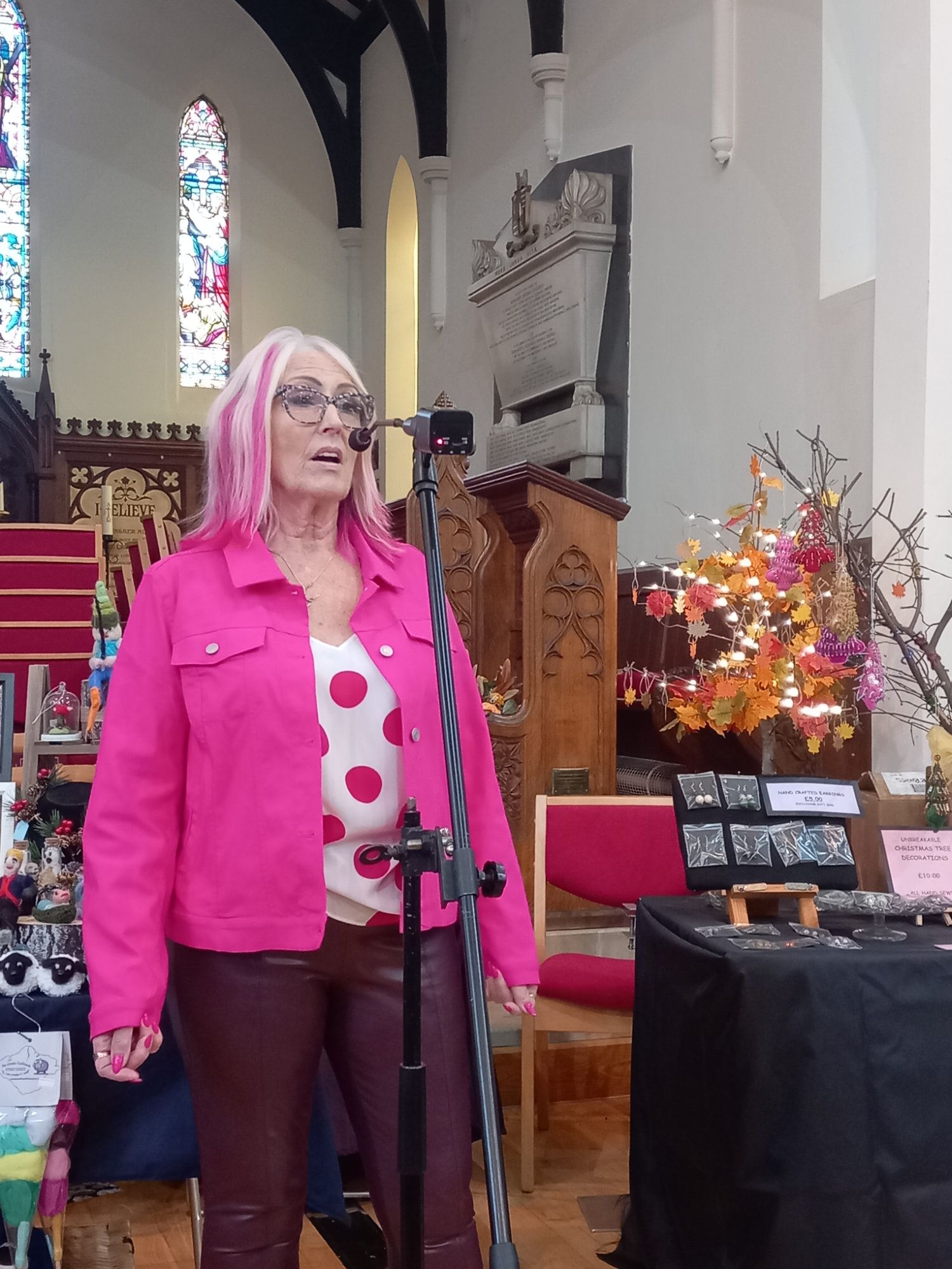 A woman with pink hair is singing into a microphone in a church.