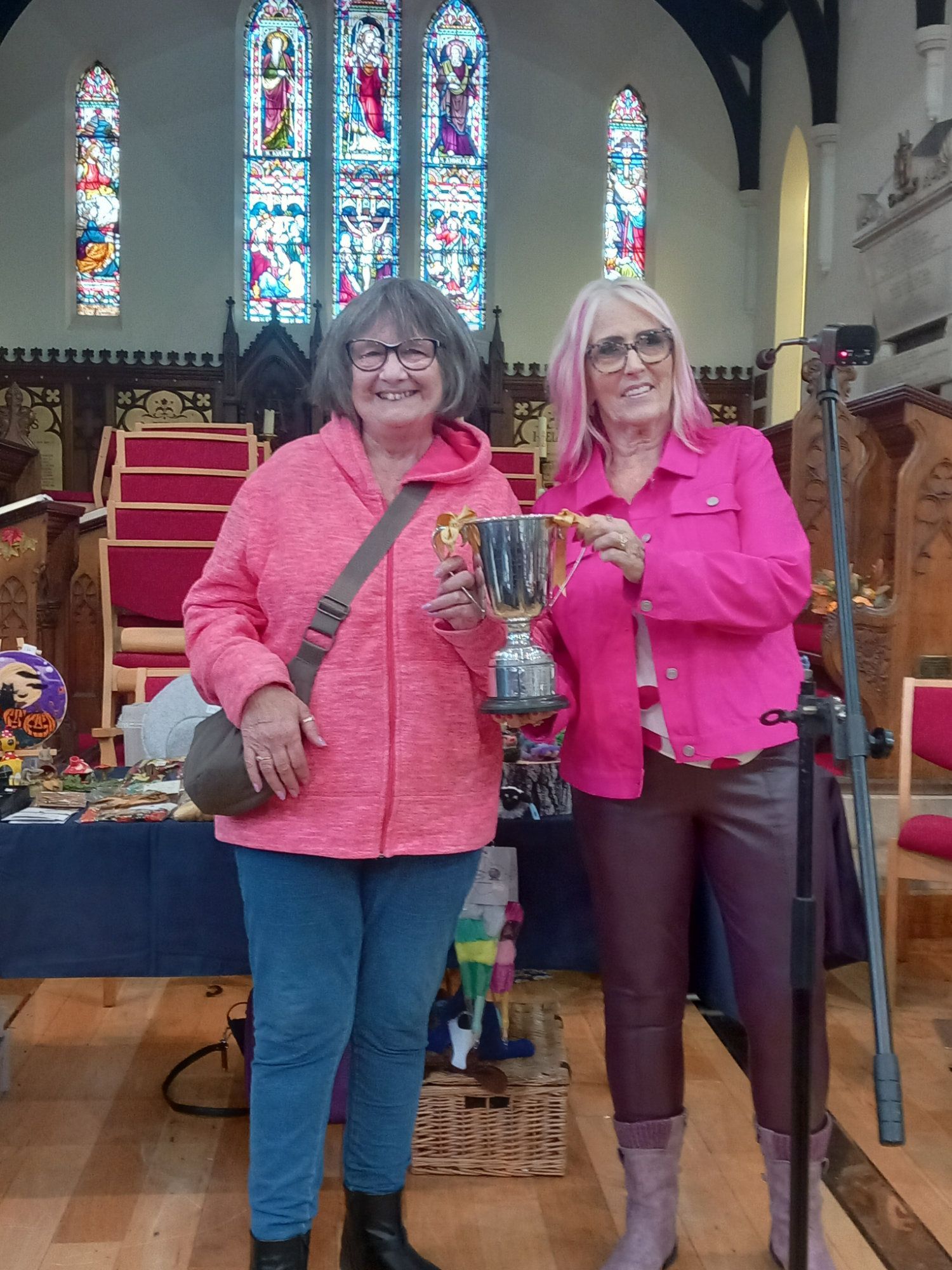 Two women are standing next to each other in a church holding a trophy.