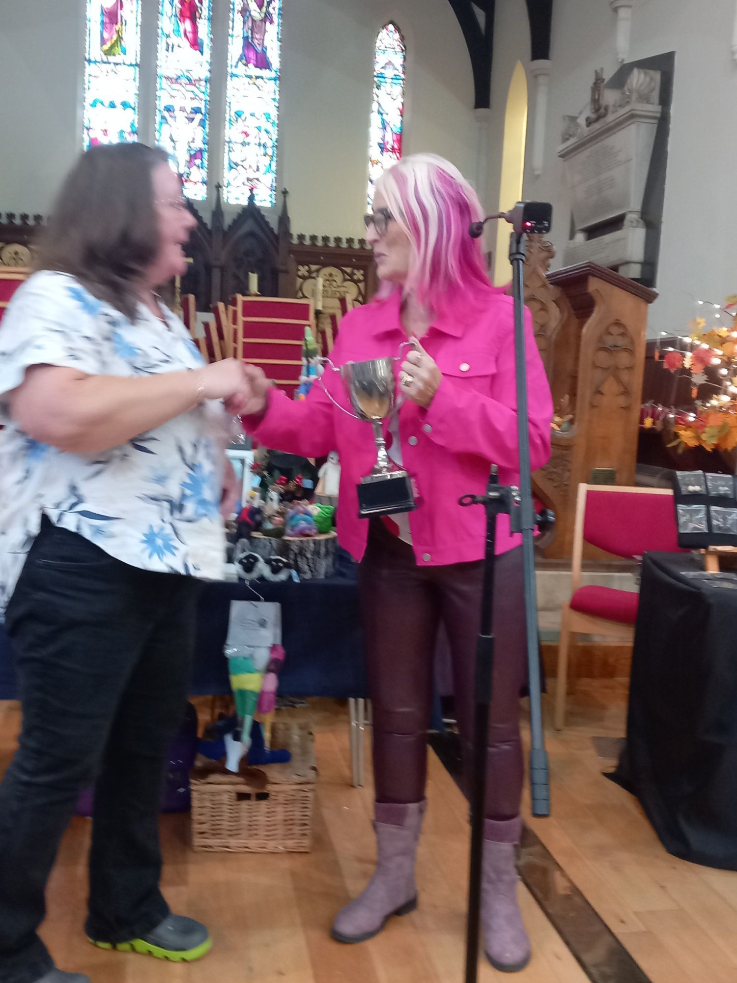 A woman in a pink jacket is holding a trophy