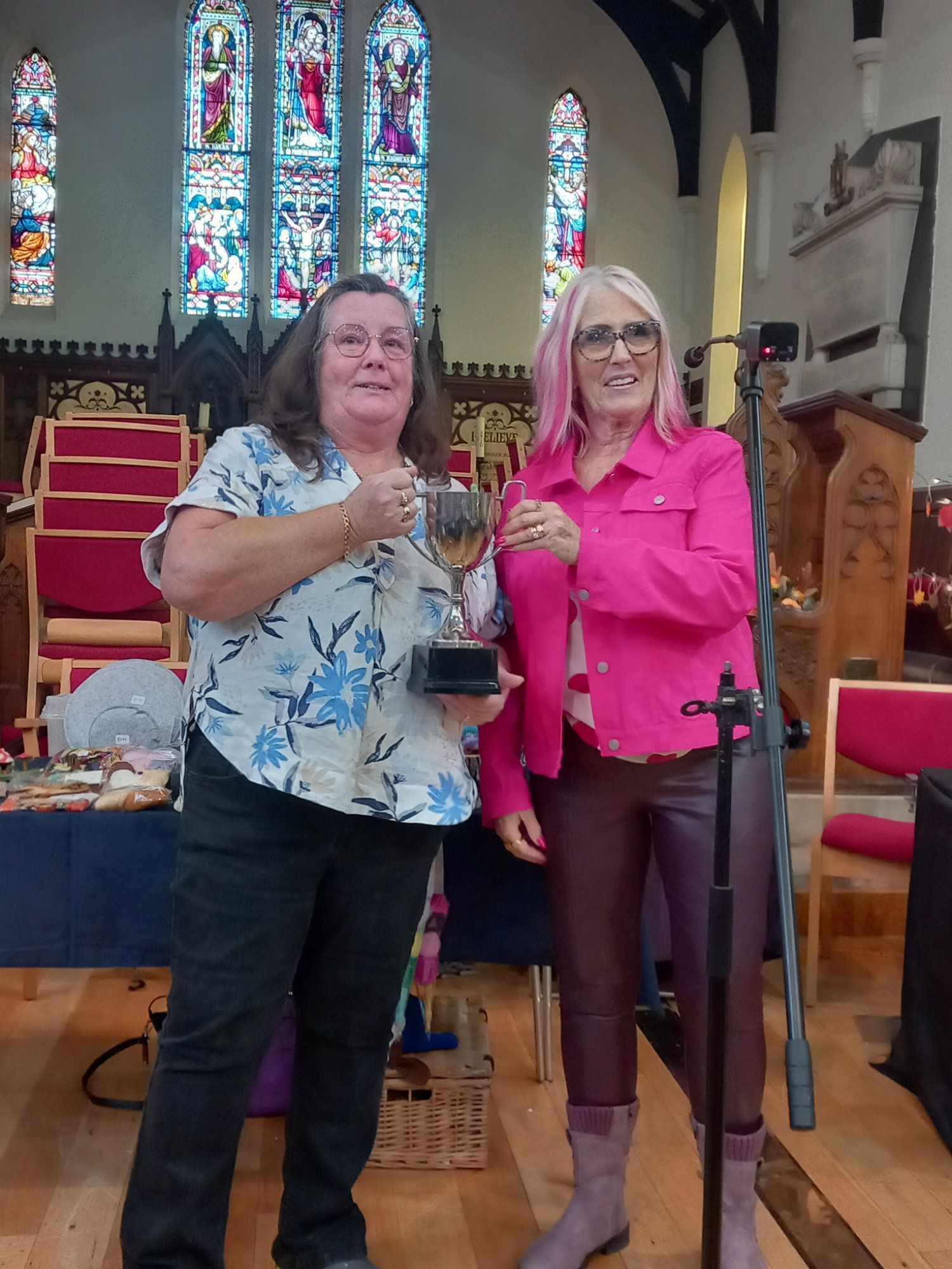 Two women are standing next to each other in a church holding a trophy.